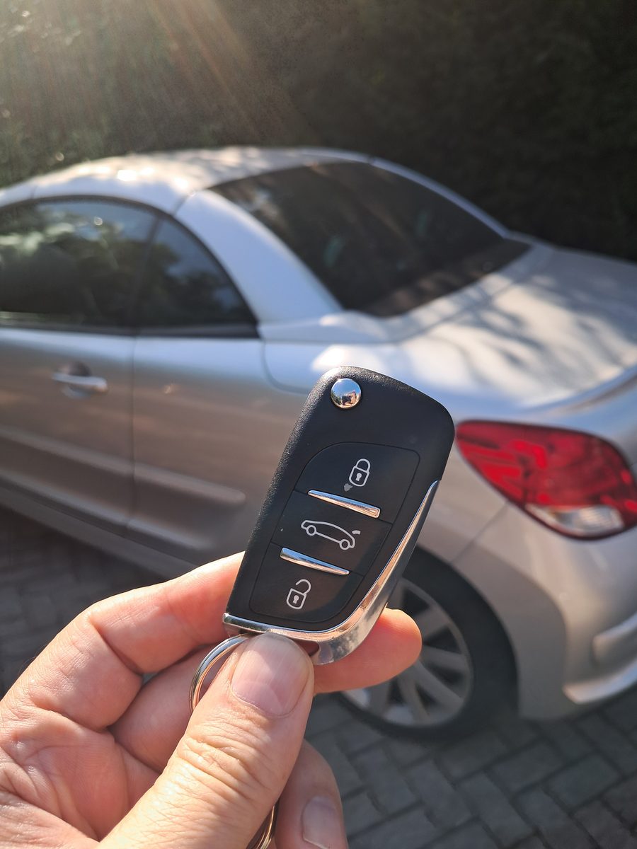 Handing over a newly cut replacement car key in front of the customer's car